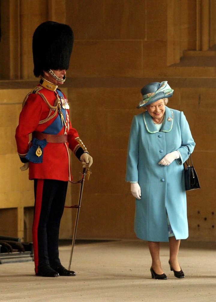 Ratu Elizabeth II tak bisa menahan senyum saat melewati Pangeran Philip yang memakai topi bulu (2005). Photo credit: Getty Images