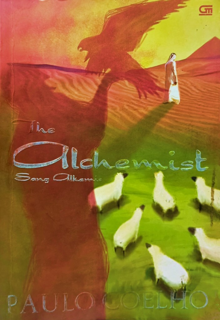 sampul bukuThe Alchemist—Sang Alkemis oleh Paulo Coelho (menggambarkan sosok pria berjubah dan bersorban putih di tengah gurun, lima ekor domba yang sedang merumput di bawahnya, piramida di kejauhan, dan bayangan raksasa seorang pria sedang memegang burung di sebelah kiri) © Gramedia Pustaka Utama